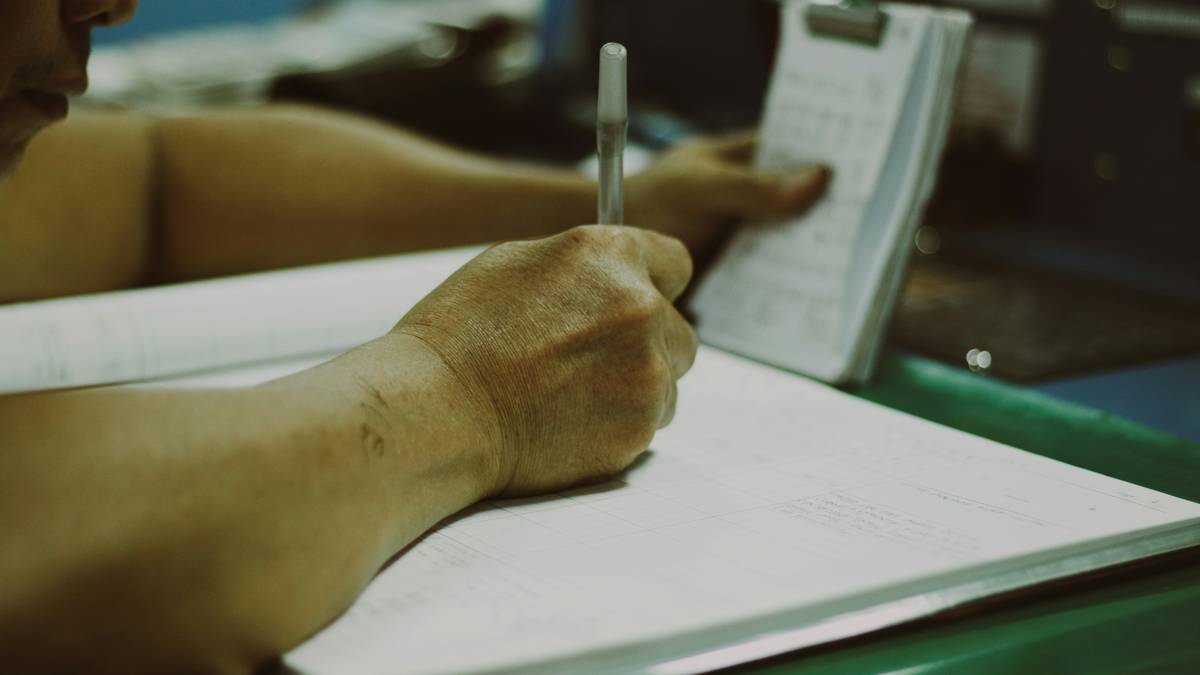 A close-up photo of someone filling out a baggage insurance claim form with a pen and documents spread across a table.